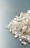 Loose diamonds on a table being picked up by a hand holding jewelry tweezers